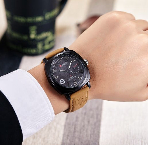 Person wearing a black wristwatch with a brown leather strap on a blurred background