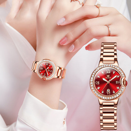 Rose gold watch with red face on a hand against a light background