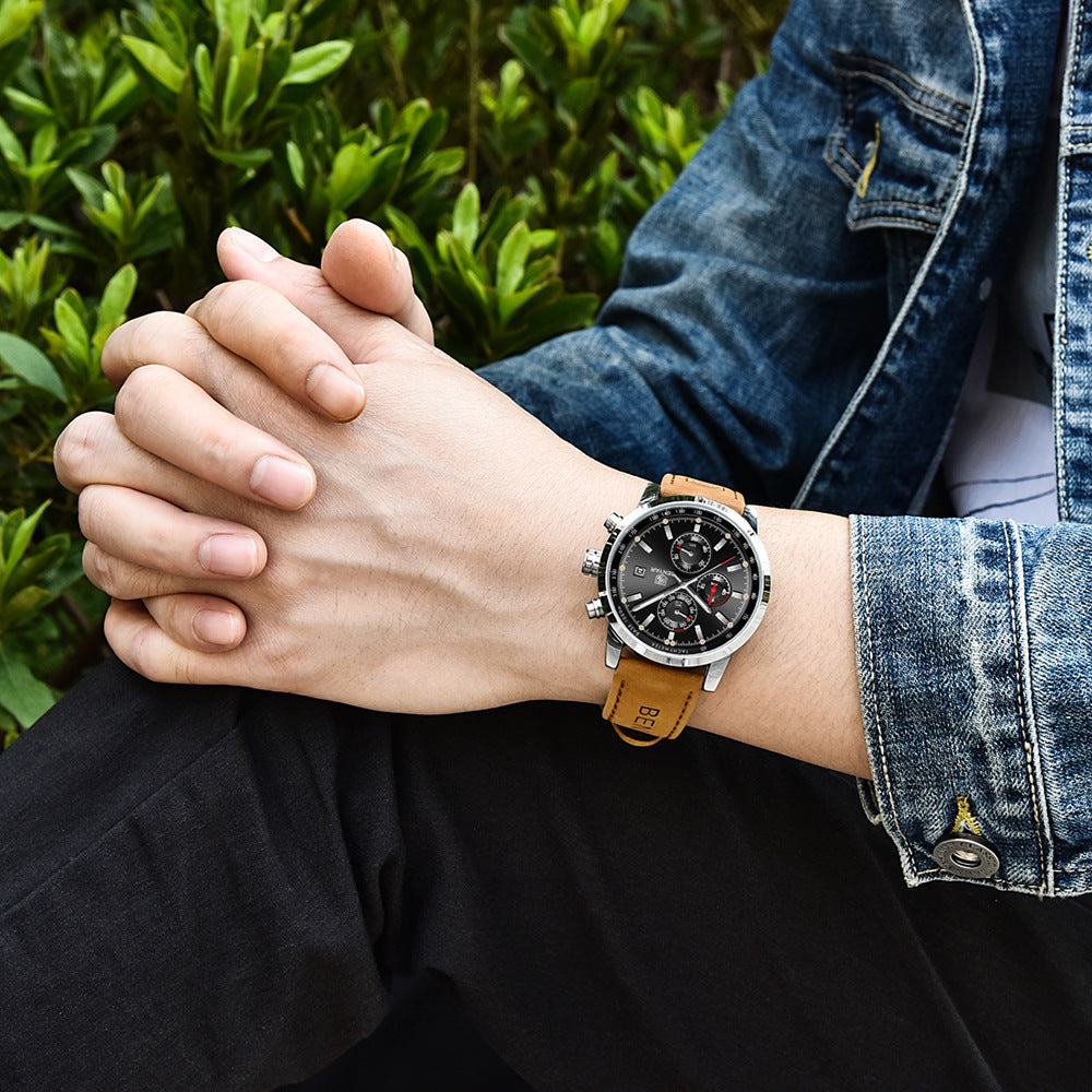 Person wearing a watch with a brown leather strap, sitting outdoors with greenery in the background.