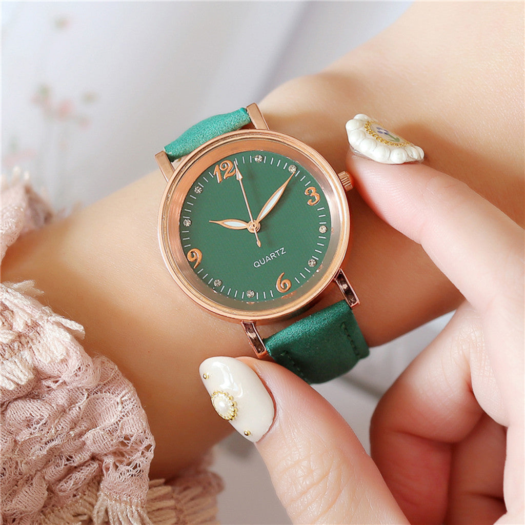 Green watch with rose gold case on a wrist against a neutral background