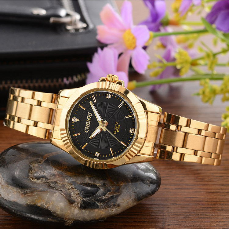 Gold wristwatch with black dial on a stone surface with flowers in the background