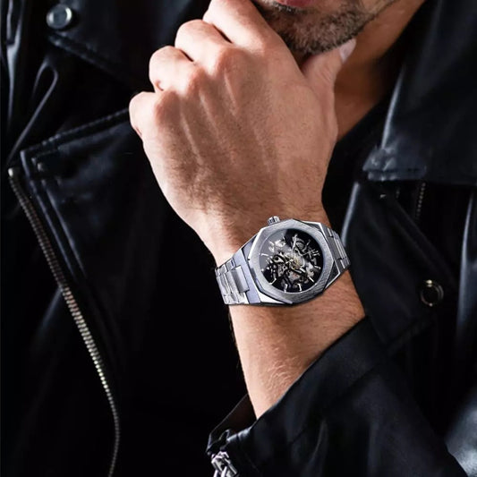 Close-up of a wrist wearing a silver watch with a black face, against a dark background.